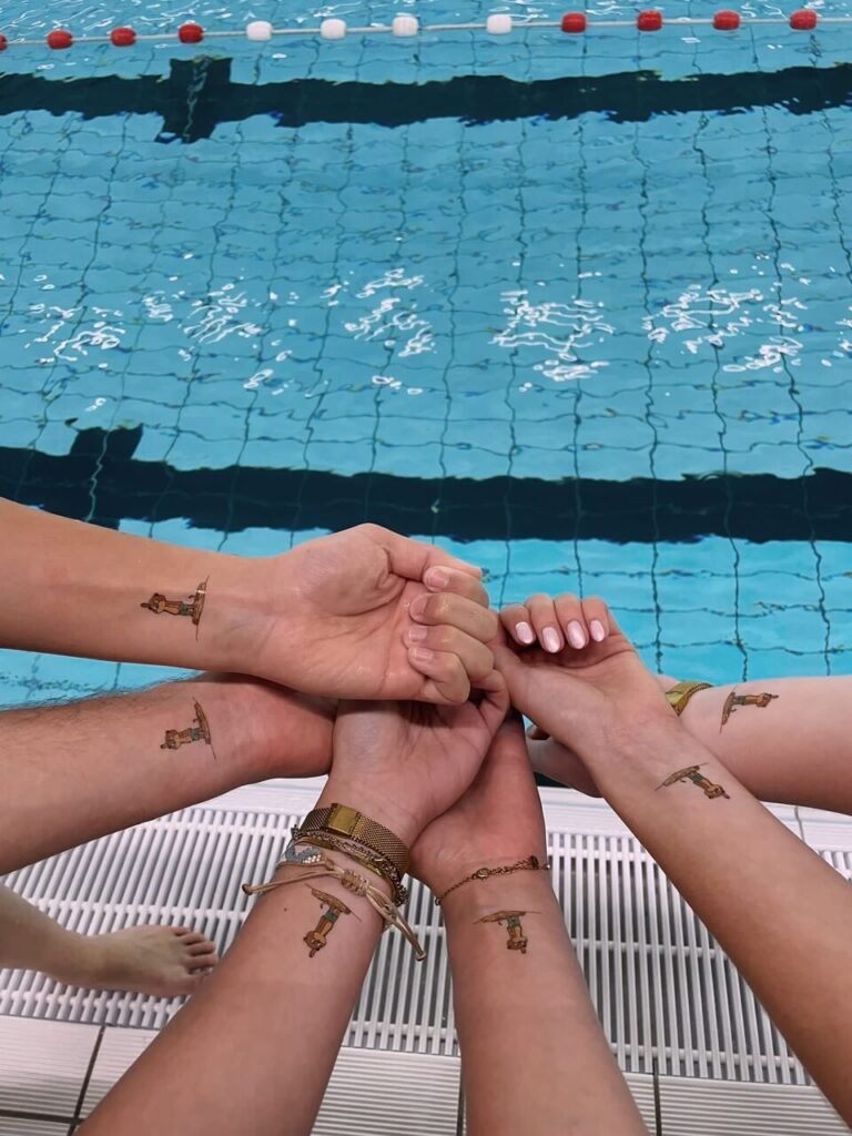 Seis muñecas al borde de la piscina, cada una con el mismo tatuaje temporal personalizzato